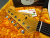 Close-up of Fender Stratocaster headstock with tuning pegs and strings in a yellow plush guitar case, showing Fender logo and serial number tag.