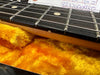 Close-up of electric guitar neck and fretboard with metal strings resting on vibrant orange plush guitar case lining.