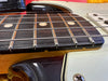 Close-up of electric guitar fretboard and strings showing wood grain, metal frets, and pickguard with screw details