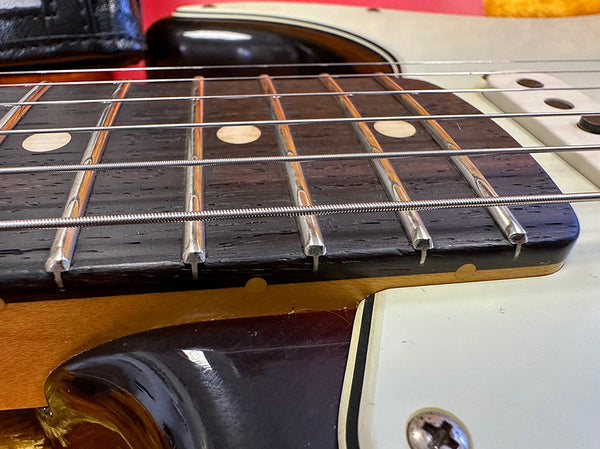 Close-up of electric guitar fretboard and strings showing wood grain, metal frets, and pickguard with screw details