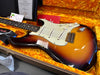 Fender Stratocaster electric guitar in sunburst finish with white pickguard and three single-coil pickups displayed in orange plush-lined hard case with Fender certificates and accessories.