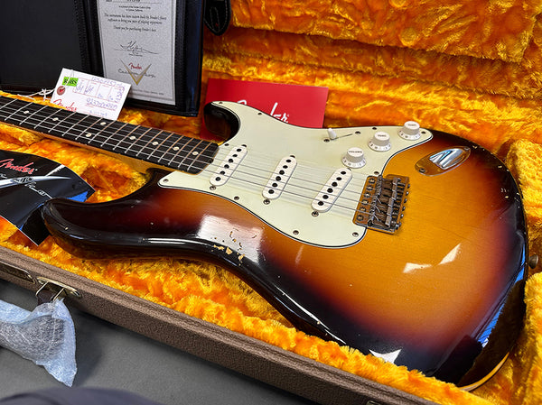 Fender Stratocaster electric guitar in sunburst finish with white pickguard and three single-coil pickups displayed in orange plush-lined hard case with Fender certificates and accessories.