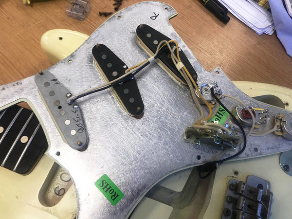 Close-up of vintage Fender Stratocaster guitar pickguard showing three single-coil pickups, wiring, and potentiometers on an aged cream electric guitar body.
