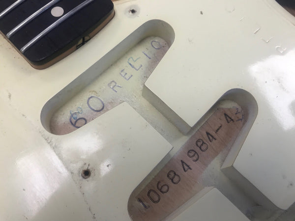 Close-up of vintage Fender guitar body cavity showing handwritten "ORELIO" and serial number 10684984-42 under white finish near black pickup and fretboard inlay