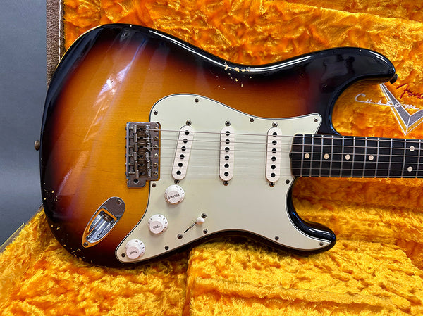Vintage Fender Stratocaster electric guitar in sunburst finish with white pickguard and three single-coil pickups resting on an orange plush lined case