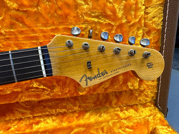 Close-up of Fender Stratocaster headstock with six tuning pegs, natural wood finish, and original contour body logo, displayed on bright orange plush guitar case interior.