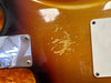 Close-up of sunburst electric guitar body showing worn finish and scratched paint near metal bridge plate and white plastic backplate screws.
