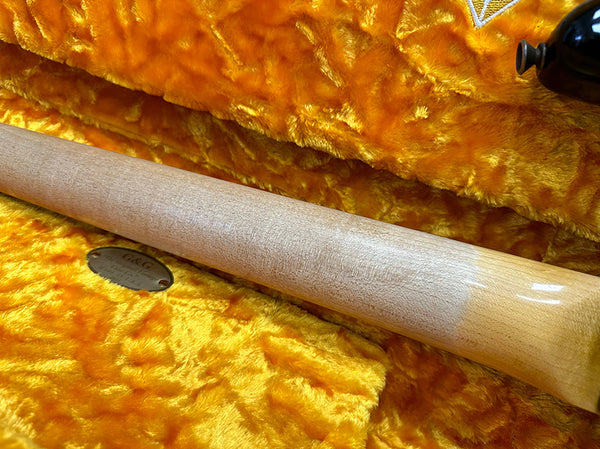 Close-up of guitar neck with satin finish resting on plush orange guitar case interior, featuring partial view of tuning peg and case label