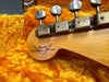 Close-up of vintage Fender Custom Shop guitar headstock with metal tuning pegs on plush orange guitar case lining