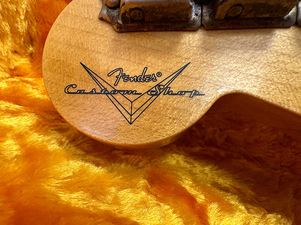 Close-up of Fender Custom Shop logo on natural wood guitar body resting on orange plush fabric case lining