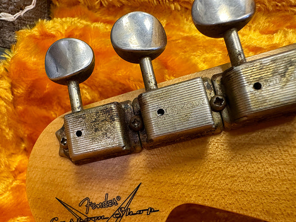 Close-up of vintage Fender Custom Shop guitar tuning pegs and headstock on a wooden guitar neck with orange plush case interior.