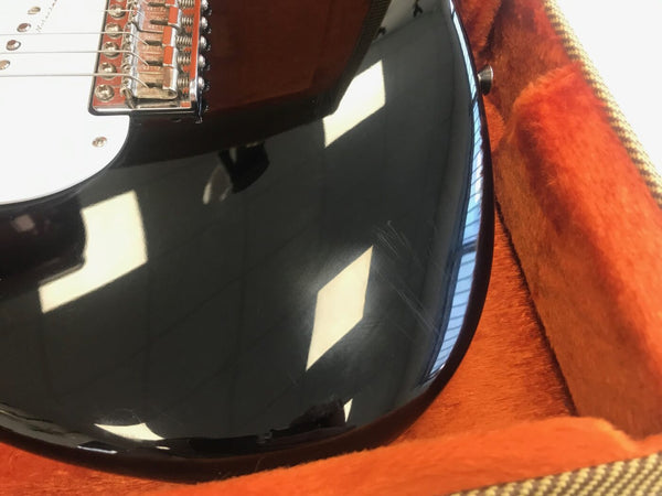 Close-up of black electric guitar body with scratches, white pickguard, and bridge, resting in orange plush guitar case interior