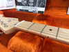 Closeup of Fender guitar maple neck and fretboard with strings inside orange plush guitar case with owner's manual in background