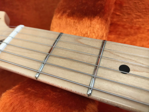 Close-up of maple guitar neck fretboard with metal frets and steel strings on orange plush background