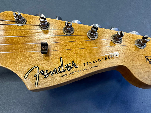 Close-up of natural wood Fender Stratocaster guitar headstock with six tuning pegs and visible strings against a dark background