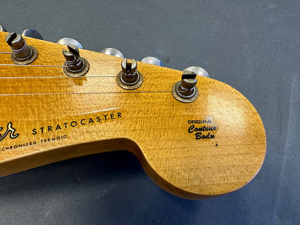 Close-up of vintage Fender Stratocaster guitar headstock with original contour body decal and tuning pegs on a gray surface