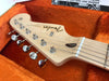 Close-up of Fender Stratocaster guitar headstock with chrome tuning pegs inside an orange plush-lined guitar case
