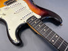 Close-up of sunburst electric guitar body and rosewood fretboard with white pickguard and single coil pickups on gray background