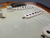 Close-up of electric guitar body showing white pickups, tone knob, and strings on sunburst finish guitar.