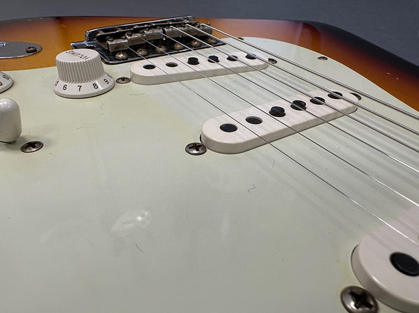 Close-up of electric guitar body showing white pickups, tone knob, and strings on sunburst finish guitar.