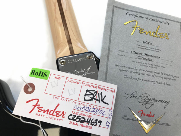 Close-up of Fender Custom Shop Clapton Stratocaster guitar neck plate with serial number CZ524639, including Fender certificate of authenticity and Fender branded tag with product details and inspection stamps.