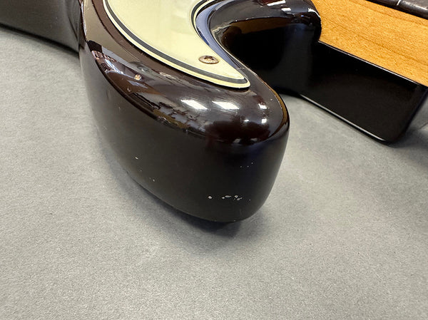 Close-up of dark brown electric guitar body corner with visible wear and scratches on gray surface