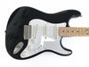 Black electric guitar with white pickguard and maple fretboard, three single-coil pickups, volume and tone control knobs, and chrome hardware on white background