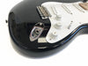 Close-up of black electric guitar body showing volume and tone control knobs, white pickguard, and chrome output jack socket on glossy finish