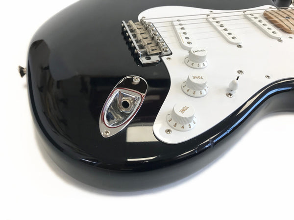 Close-up of black electric guitar body showing volume and tone control knobs, white pickguard, and chrome output jack socket on glossy finish