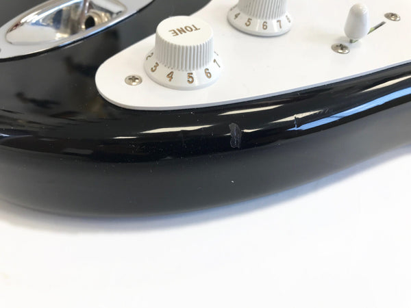 Close-up of black electric guitar body showing tone control knob and paint chip damage near the pickguard