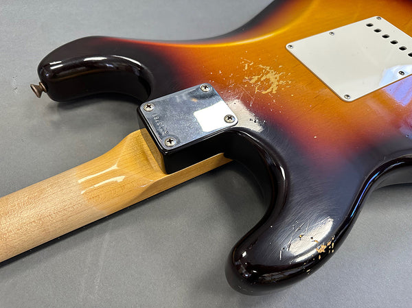 Close-up of vintage sunburst electric guitar body and neck joint with visible wear and aging on finish, showing metal neck plate and wooden neck on gray background.