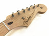 Close-up of natural wood Fender Stratocaster electric guitar headstock with tuning pegs and strings on white background
