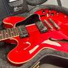 Close-up of bright red semi-hollow body electric guitar with dual humbucker pickups and black pickguard inside a gray plush guitar case