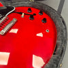 Close-up of red electric guitar body with black control knobs, cream toggle switch, and chrome bridge, resting in a plush gray guitar case.
