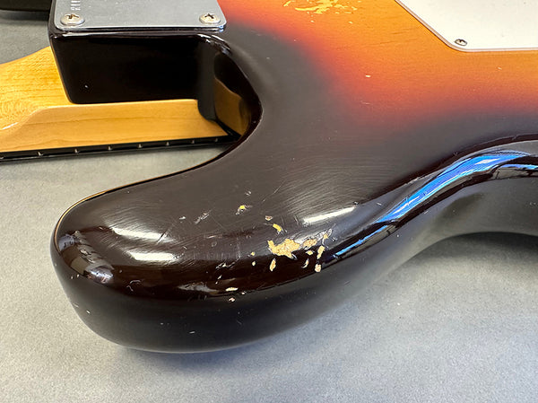 Close-up of worn and chipped sunburst finish on the back lower bout of an electric guitar body with a maple neck heel and neck plate screws visible on gray surface at Coffee House Guitars.