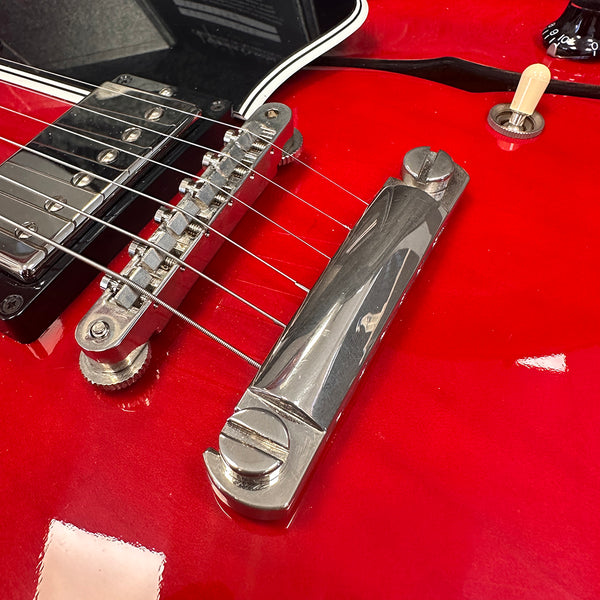 Close-up of red electric guitar bridge and tailpiece with metal strings and toggle switch on glossy finish body
