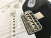Close-up of black and white electric guitar bridge with Fender saddles and white tone and volume knobs on white pickguard