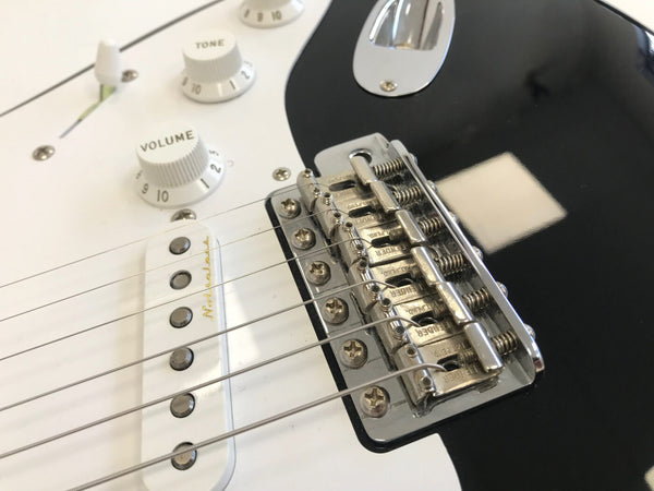 Close-up of black and white electric guitar bridge with Fender saddles and white tone and volume knobs on white pickguard