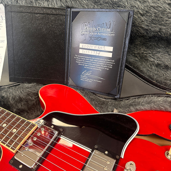 Gibson Custom Certificate of Authenticity displayed in open black folder with red electric guitar and black pickguard in case interior with gray plush lining