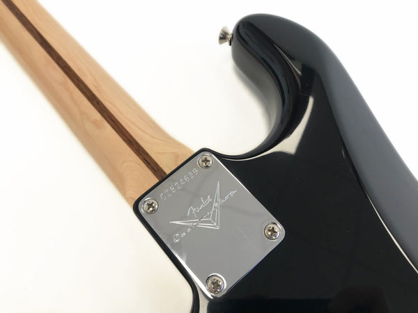 Close-up of Fender Custom Shop stamped neck plate on black electric guitar with maple neck and walnut stripe