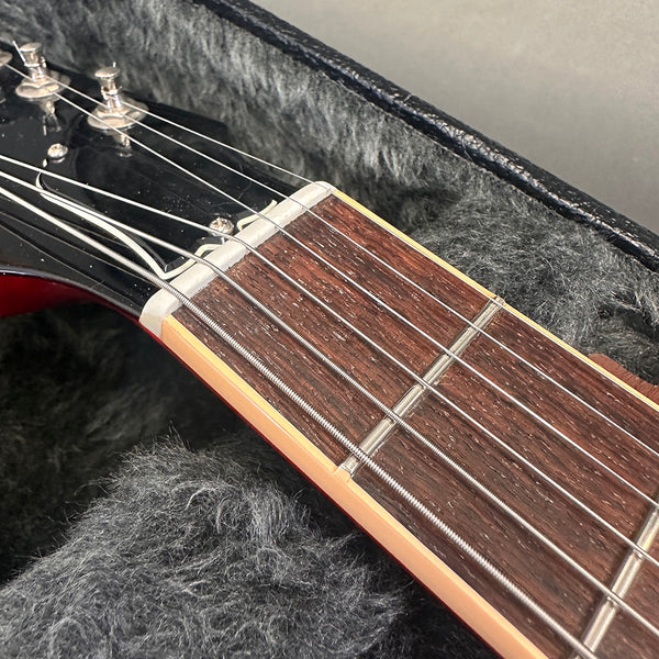 Close-up view of guitar neck and fretboard with steel strings in black hard case with gray plush lining.