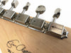 Close-up of vintage-style metal tuning pegs on light wood guitar headstock with signature and model text visible