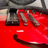 Close-up of red semi-hollow electric guitar body showing chrome bridge, tailpiece, black pickup, control knobs, and f-hole design in guitar case lining