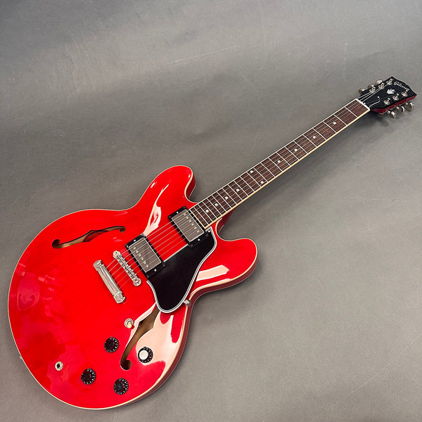 Red Gibson semi-hollow electric guitar with black pickguard and dual humbucker pickups on gray background