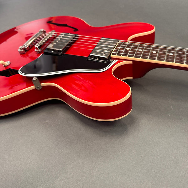 Close-up of red semi-hollow body electric guitar with black pickguard and dual humbucker pickups on gray background