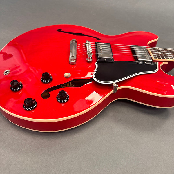 Close-up of a red semi-hollow electric guitar body with black pickguard, two humbucker pickups, four control knobs, and a chrome bridge on a gray background
