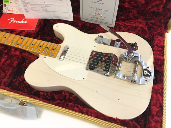 Fender electric guitar with Bigsby vibrato tailpiece, maple neck, and white pickguard, resting in red velvet-lined guitar case with Fender owner’s manual and certificate of authenticity.