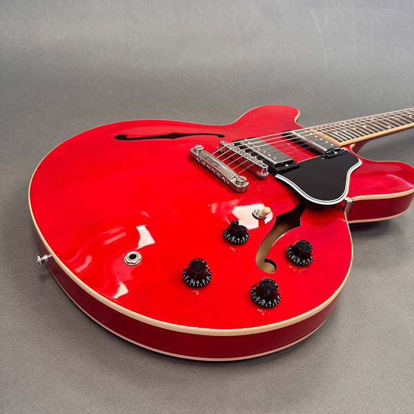 Red semi-hollow electric guitar with black pickguard, chrome bridge, four black control knobs, and cream binding on gray background