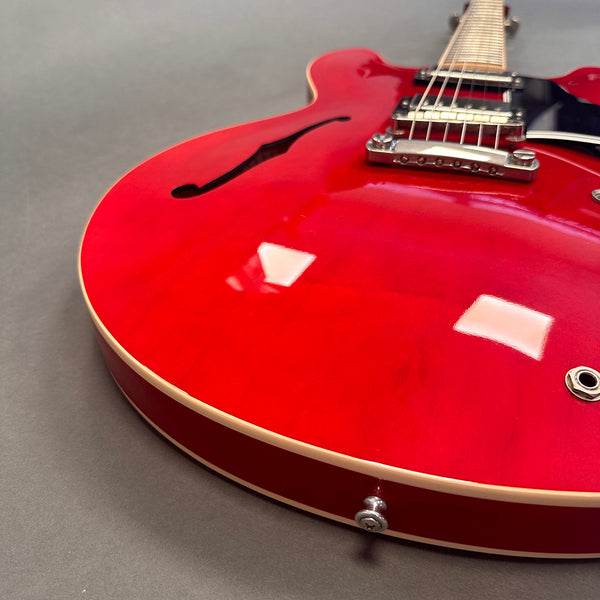 Close-up of red semi-hollow electric guitar body with f-hole and chrome hardware on gray background