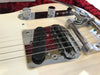 Close-up of white electric guitar bridge, chrome saddles, black pickup, metal control knobs, and strings on red plush guitar case background